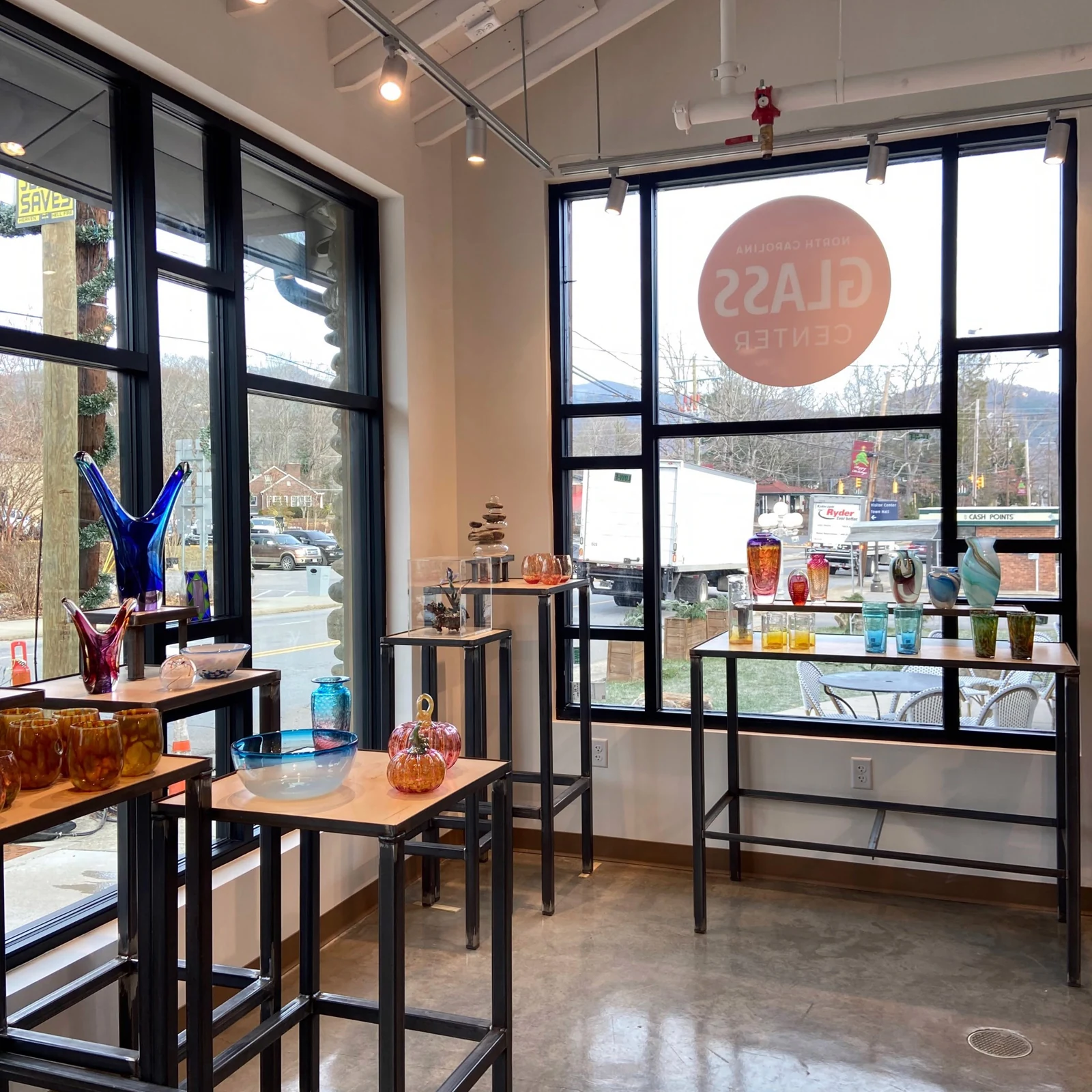 Finished North Carolina Glass Center gallery with glass artworks displayed beside tall street-facing windows