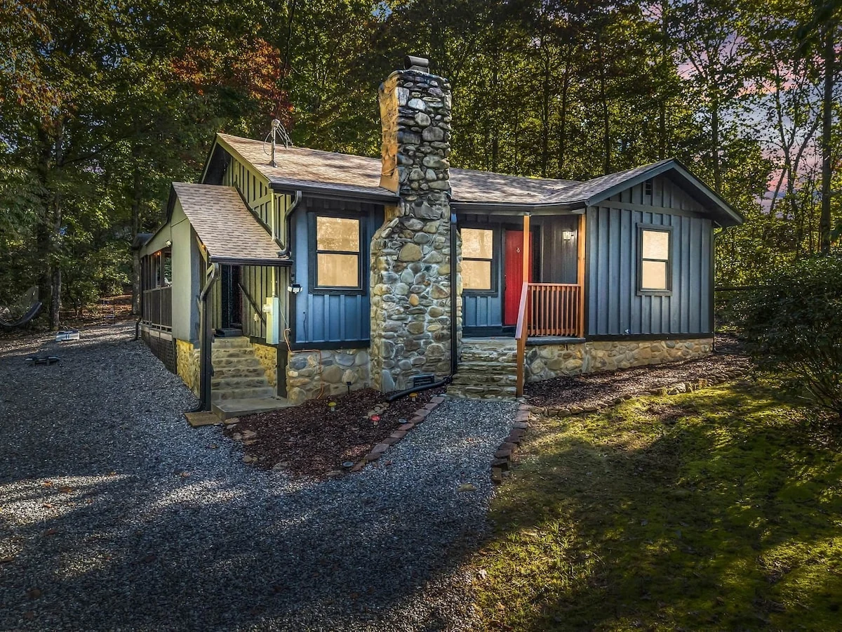 Stonehaus after renovation, with dark siding, a stone chimney and a wooded setting