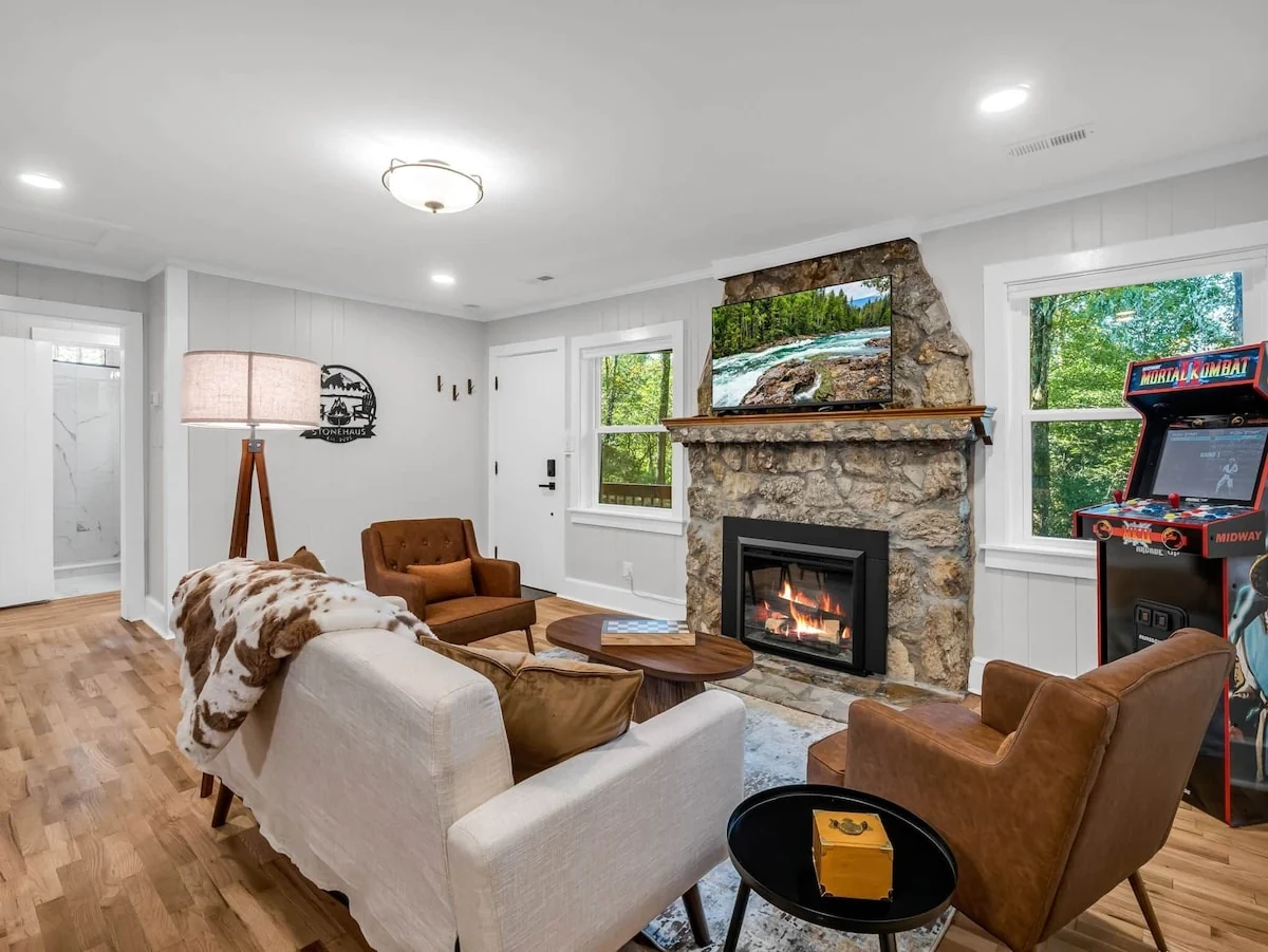 Finished Stonehaus living room with a stone fireplace, warm seating and an arcade cabinet